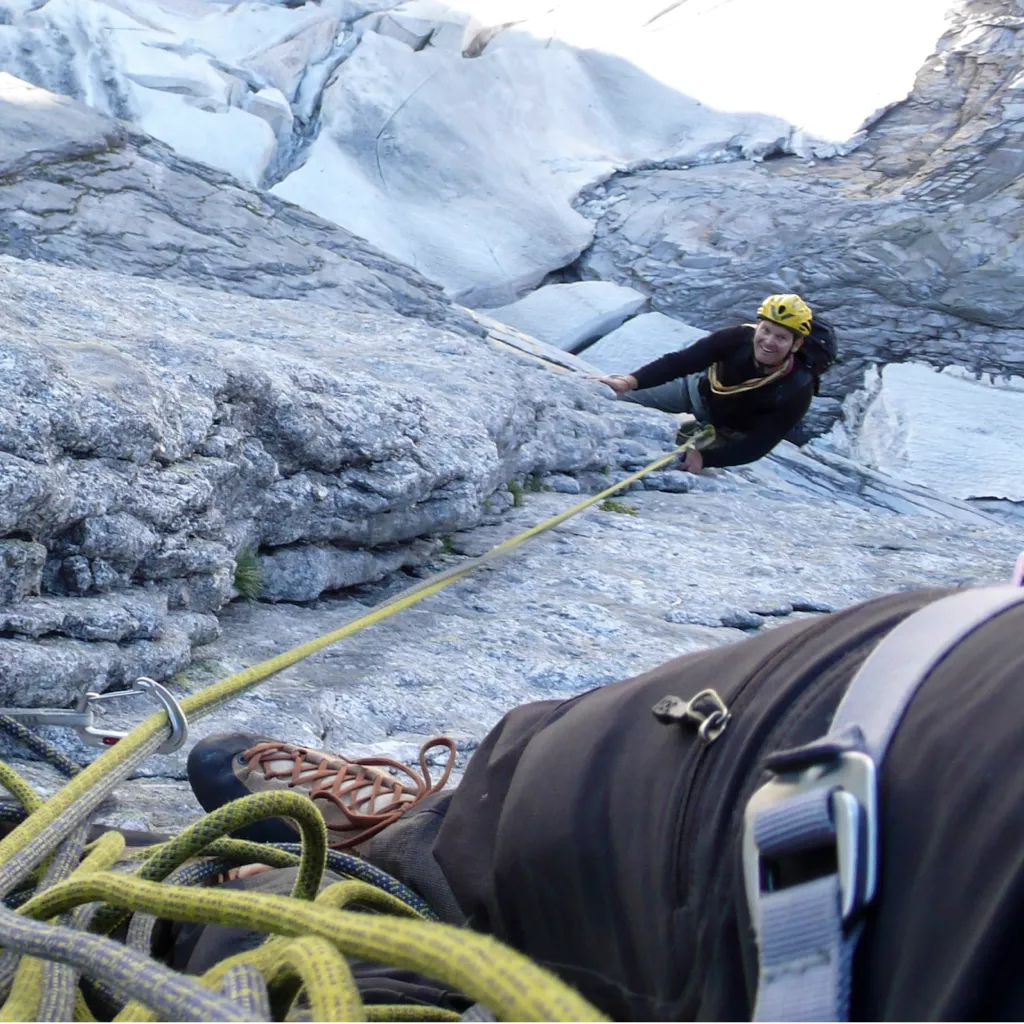 Man on a rope, climbing a mountain.