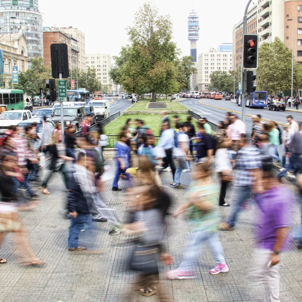 A local community street scene with lots of people crossing a road.