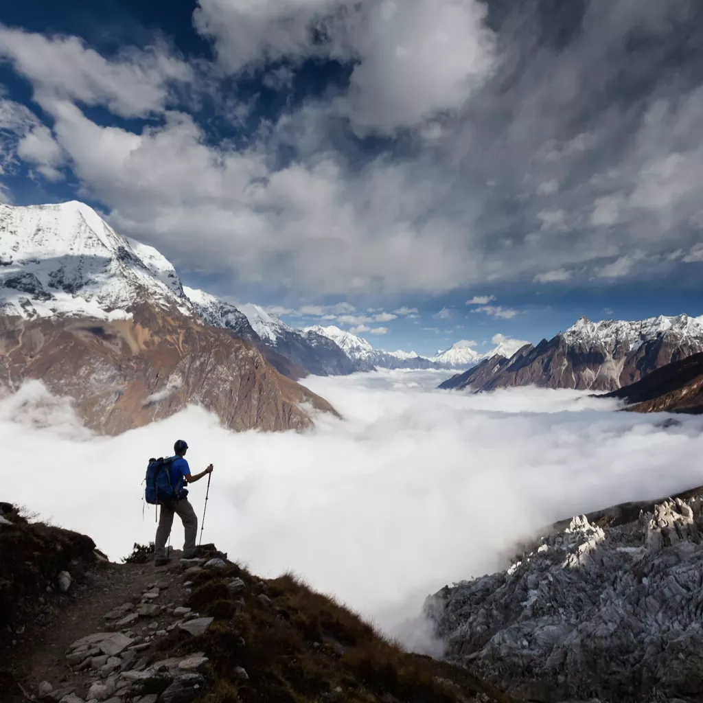 Man stood on top of a mountain, looking down on clouds.