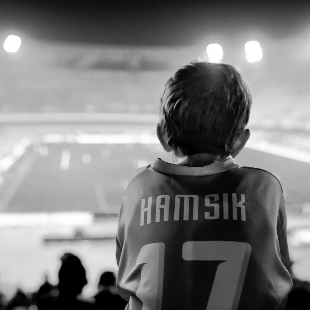 A boy is watching his heroes at a football match.