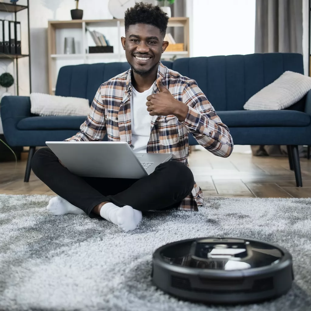 A man works while a robot vacuum cleaner cleans.