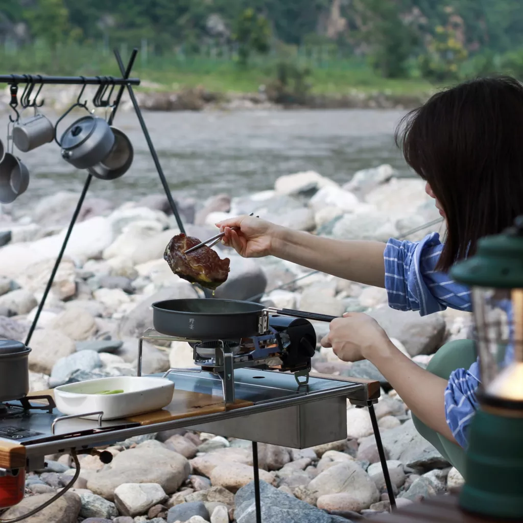 A lady cooking on a gas camping fire.