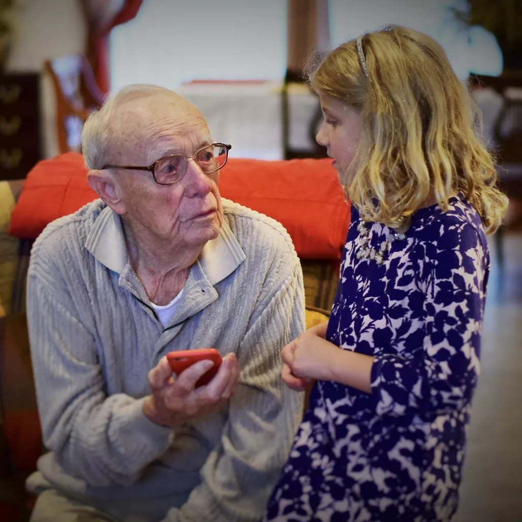 A grandfather showing his phone to his granddaughter.