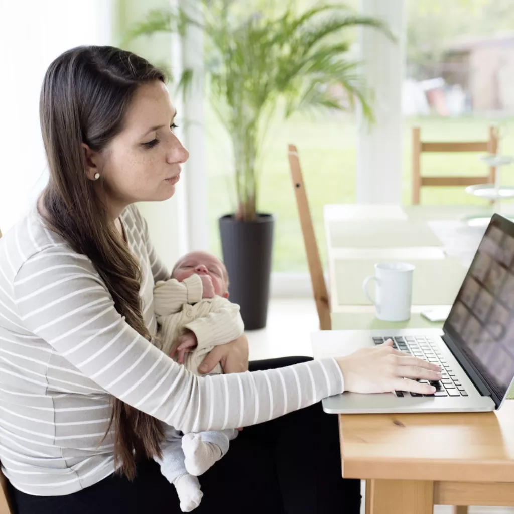 A mother with a baby on her lap, working on her computer.
