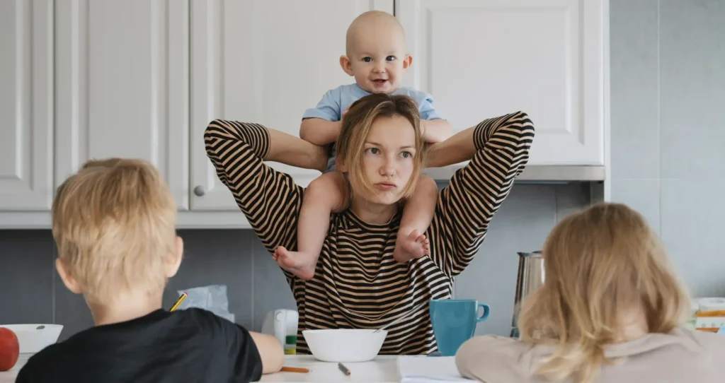 An exhausted mother with her children all around her at the breakfast table.