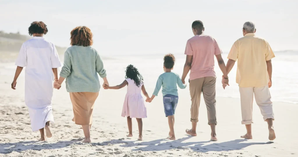 A large family group, hand in hand, walking along the beach.